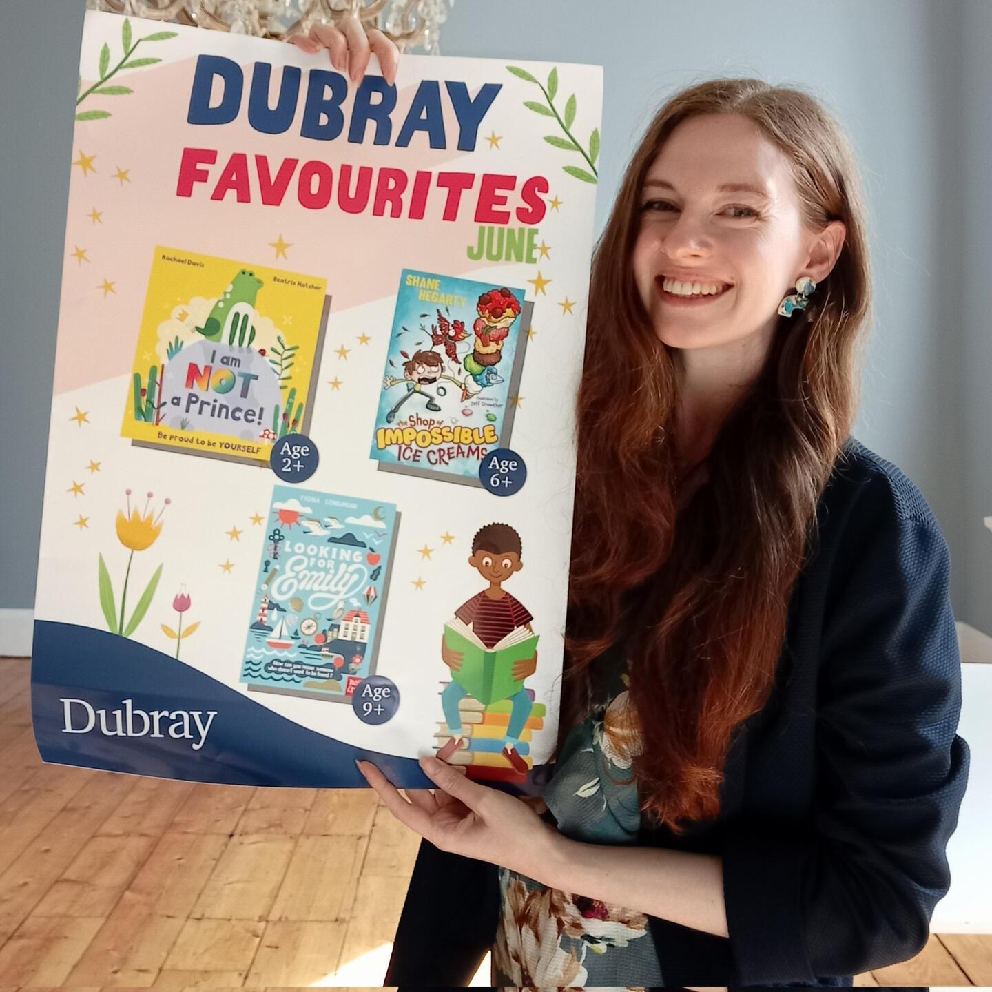 Fiona is holding a Dubray poster showing their June favourites: I Am Not A Prince, the Shop of Impossible Ice Creams and Looking for Emily